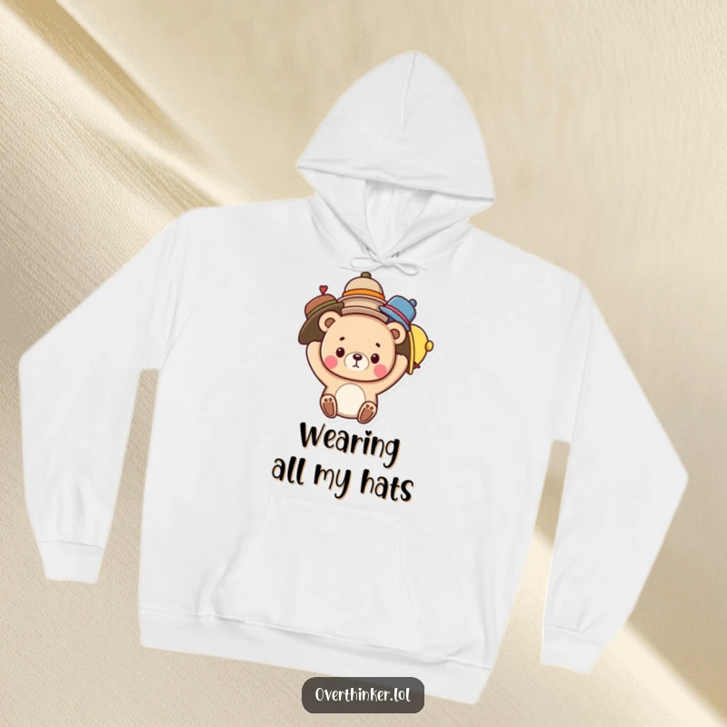 Funny hoodie depicting a cute bear character struggling to keep multiple hats balanced on its head, a humorous take on multitasking.